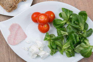 Tomato salad and heart shaped ham on wooden table