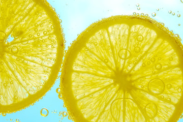 Fresh lemon slice in water with bubbles on sky background