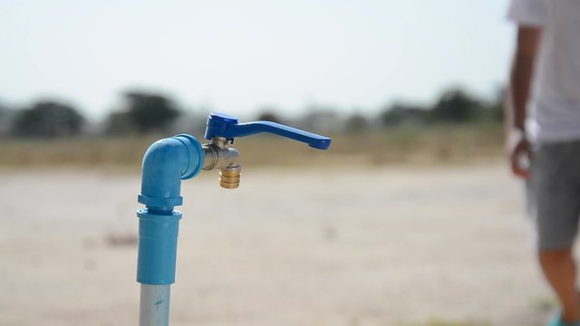 Water shortage concept.Close up Asian boy open metal blue water faucet on hot and dry empty land.