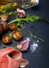 Cherry tomatoes, prosciutto, arugula and spices on black board