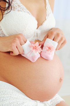 Pregnant woman in beautiful lingerie holding baby shoes on her belly