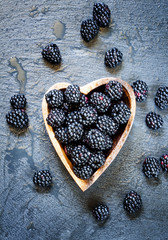 Fresh blackberries in a bowl in the shape of a heart on a dark b