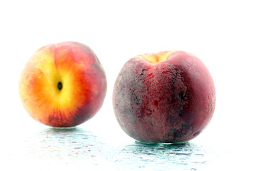 two ripe peaches in the water droplets on white background