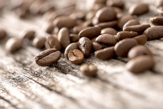 Low angle view of a heap of fresh roasted coffee beans lying on an old rustic wood surface, shallow DOF with copyspace.