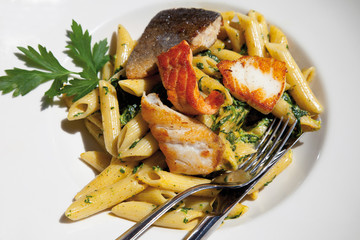 Nahaufnahme von gegrilltem Fisch gemischt mit Penne und Spinat