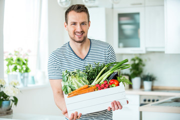 Junger Mann mit Gemüsekiste in der Küche
