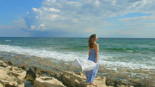 Beautiful brunette woman in maxi dress enjoying windy day on seashore, vacation