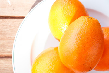 Orange on white plate put on wooden table.