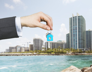 A hand is holding a key from the new home. A concept of real estate property agency. Miami cityscape on the background. - Powered by Adobe