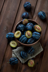 Bowl with ripe plums over dark rustic wooden background