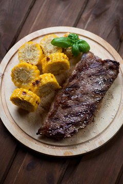 Chopping board with grilled striploin steak and sliced sweetcorn