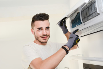 handsome young man electrician installing air conditioning in a client house