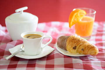 Breakfast with a cup of coffee, chocolate croissant, orange juice and a sugar bowl
