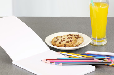 making homework: school supplies with blank notebook and glass of orange juice and chocolate chip cookies

