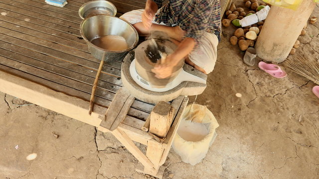 Upper view on woman sat cross-legged using hand-turned millstone to grind wet rice for making soaked rice flour