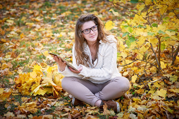 young woman with a tablet sitting in the autumn park