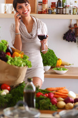 Young woman cutting vegetables in kitchen, holding a glass of