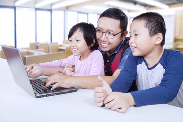 Two students using laptop in class with teacher