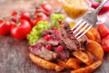 Beef with cranberry sauce, roasted potato slices and bun on cutting board, on wooden background