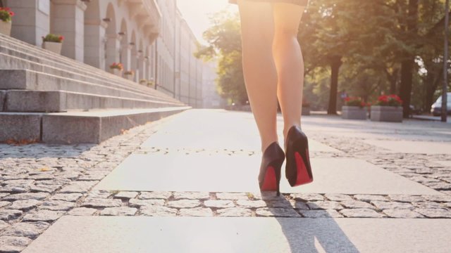 Sexy woman in black high-heeled shoes walking in the city urban street then climbs the stairs, close up on feet. Steadicam stabilized shot in Slow motion. Business woman in the morning. Lens flare. 