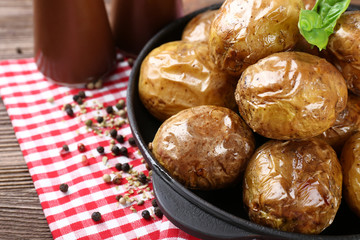 Baked potatoes in pan on wooden table, closeup