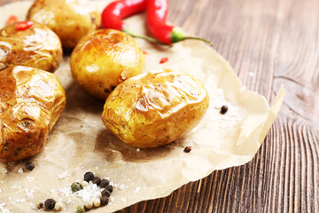 Baked spicy potatoes on parchment on wooden table, closeup