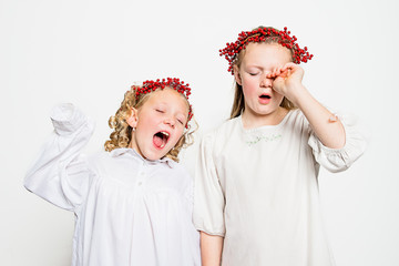 Two girls in white nightgowns yawning and wearing red berry hair wreaths