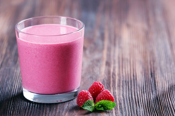Glass of raspberry milk shake with berries on wooden background