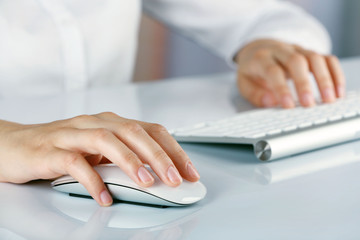 Female hands typing on keyboard and holding computer mouse on light background