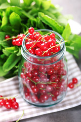 Fresh red currants in jar with mint on table close up