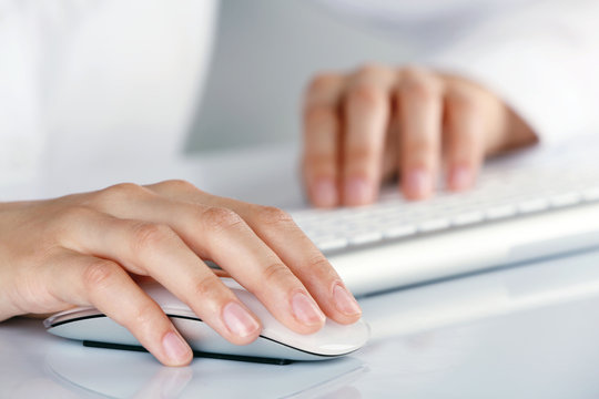 Female hands typing on keyboard and holding computer mouse on light background