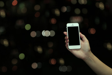 Female hand holding touch screen mobile phone on blurred night lights background