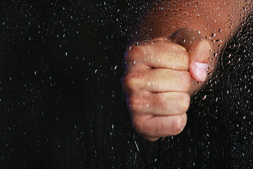 Fototapeta na wymiar Male hand behind wet glass, close-up