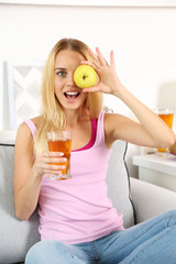 Young beautiful woman sitting on sofa with glass of fresh apple juice