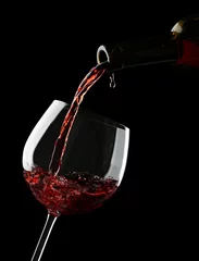 Fotobehang Rode wijn gieten in wijnglas op zwarte achtergrond © Africa Studio