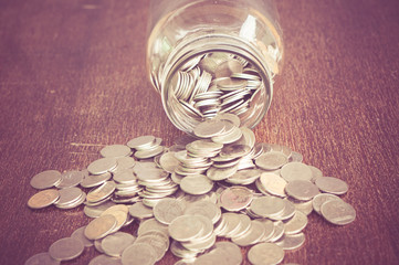 Coins spilling out of a glass bottle with filter effect retro vintage style