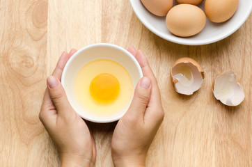 Fresh egg yolk in the bowl are holding by hand on wooden background