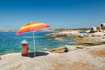 Woman in red bikini and white hat under parasol 