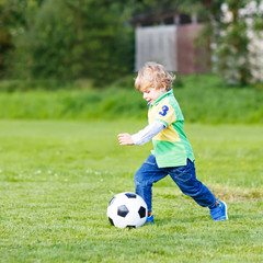 Two little sibling boys playing soccer and football on field