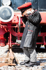 Fototapeta na wymiar Interruption of Journey / Nostalgic little child boy railroad conductor stand in front of a steam locomotive, looking down and wondering about the end of the track