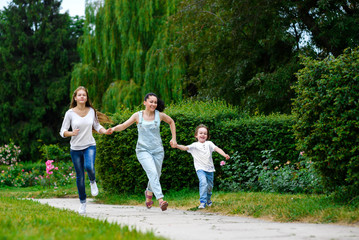 Naklejka na ściany i meble Happy Mother with daughter and son running on grass smiling