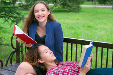 Fototapeta premium Two teenage girls reading books on bench in city park