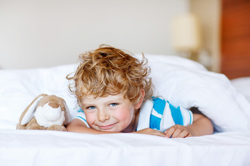 Adorable kid boy after sleeping in his white bed with toy © Irina Schmidt