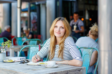 Woman drinking coffee and writing notes in cafe