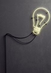 3 D render of an light bulb shaped neon light against concrete wall. Neon light is turned on and it is glowing in lighter yellow color. 