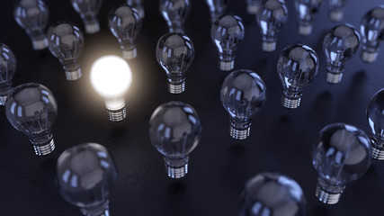 3 D render of an illuminated light bulb in a group of turned off light bulbs. The scene is very dark and only lights is coming from one light bulb.
