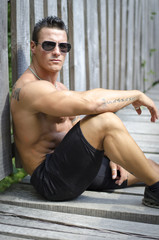 Obraz premium Handsome, serious muscleman sitting against wood fence