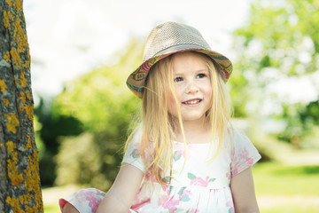 Smiling blond girl in a hat at sunny summer day in the garden.