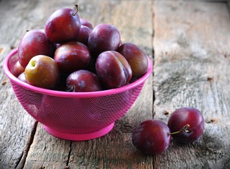 Fresh organic plums in a basket on a wooden table