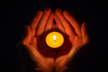 hands in the shape of a heart holding a lighted candle on a black background